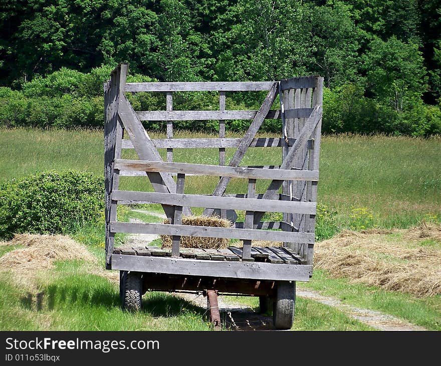 A nice hay wagon sits in a field with one bale of hay in it.