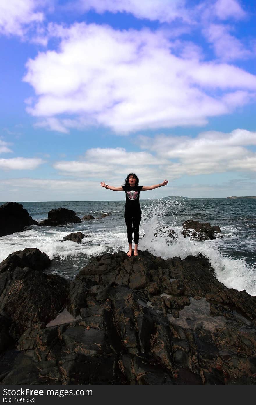 A beautiful woman doing yoga on the edge of the rocks with waves splashing to show a healthy way to live a happy and relaxed lifestyle in a world full of stress. A beautiful woman doing yoga on the edge of the rocks with waves splashing to show a healthy way to live a happy and relaxed lifestyle in a world full of stress