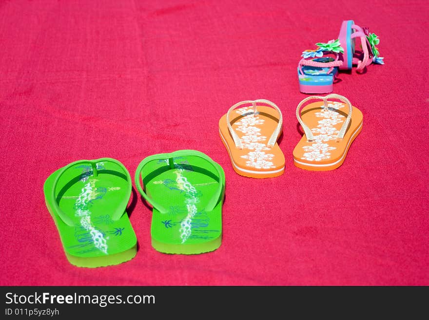 Three pairs of flipflops on red beachtowel. Symbol for dad, mum and the little daughter. Family on vacation, fun, sea and summer concept. Space for copy.