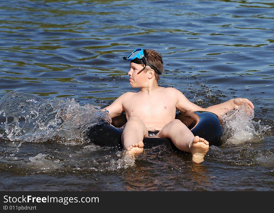 The boy sitting on a tube making splashes in a small lake.