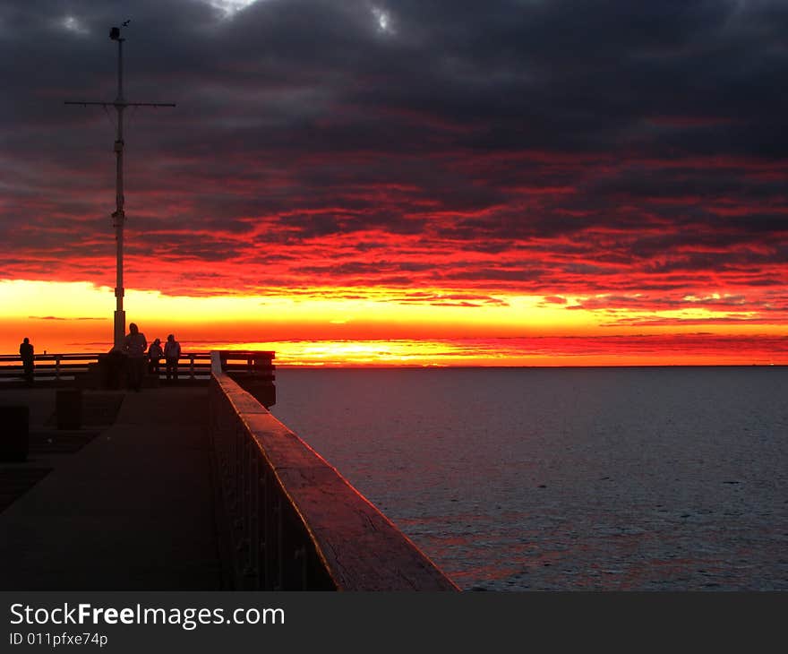 Orange clouds as the sun rises over the ocean with pier in foreground. Orange clouds as the sun rises over the ocean with pier in foreground