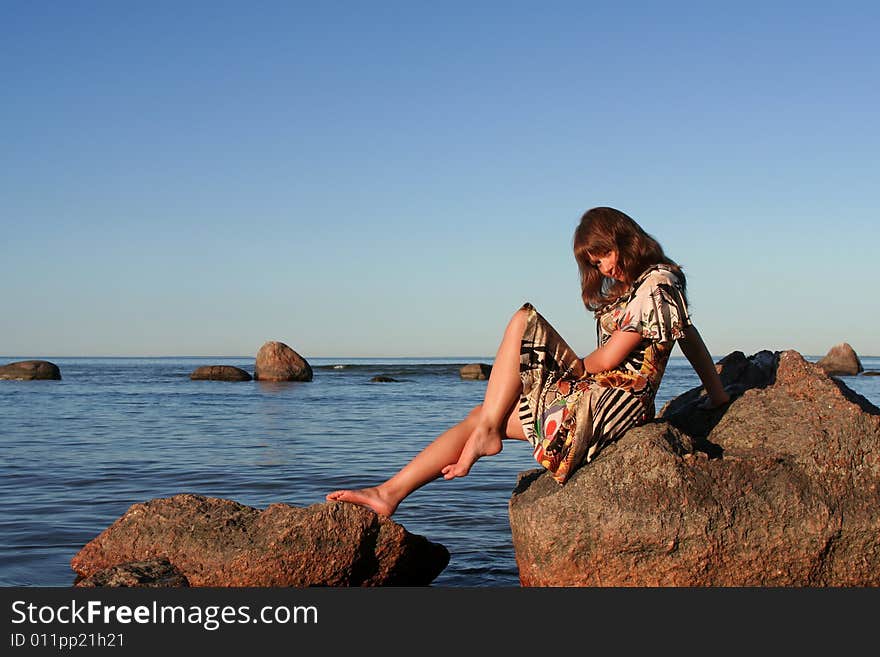 Pretty young woman sitting on a stone in the sea