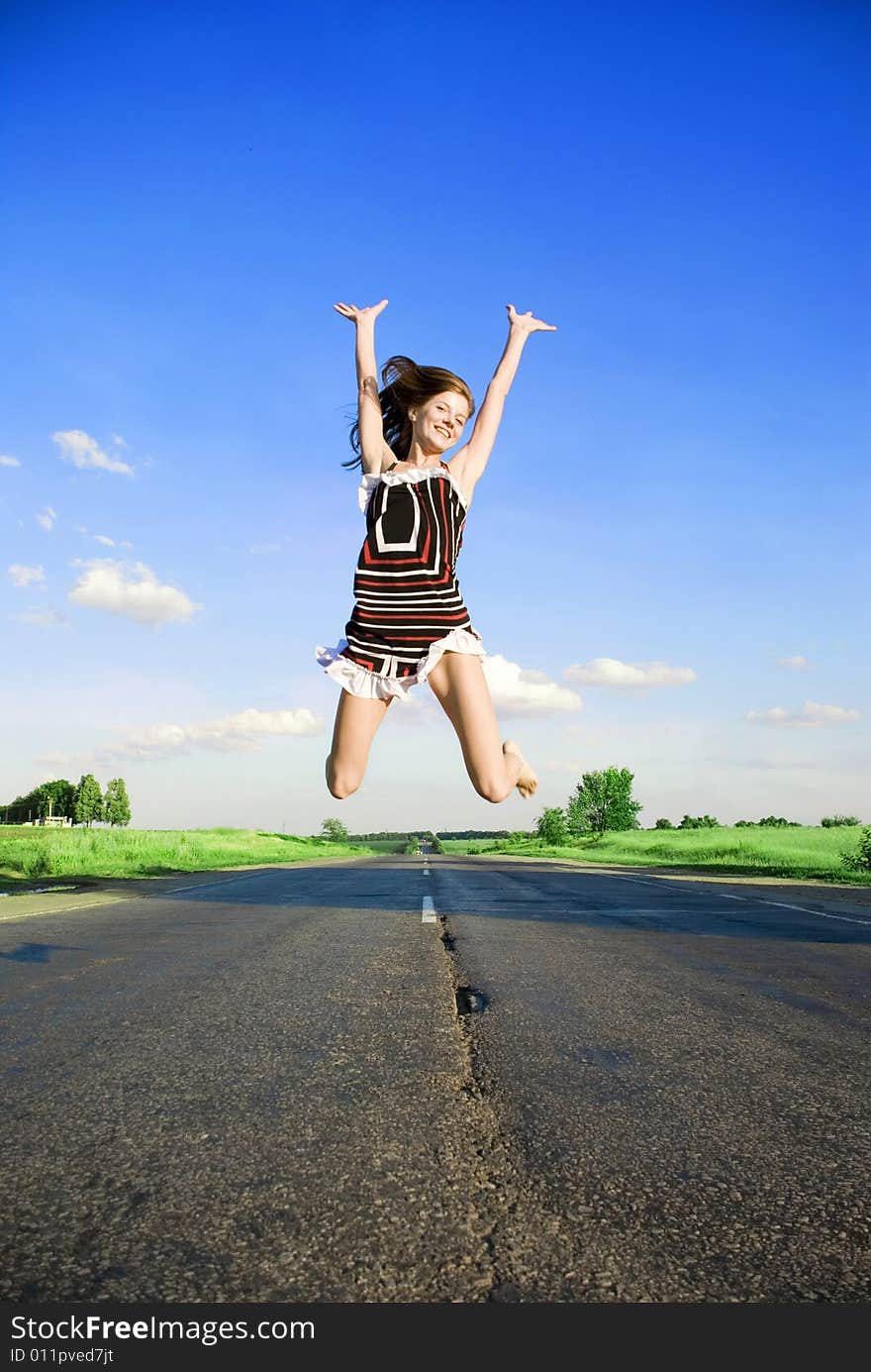 Jumping happy girl over the road under blue sky