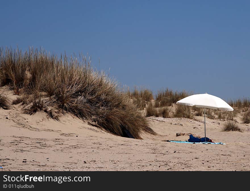 A lonely white umbrella on a sandy beach of a Greek island. A lonely white umbrella on a sandy beach of a Greek island