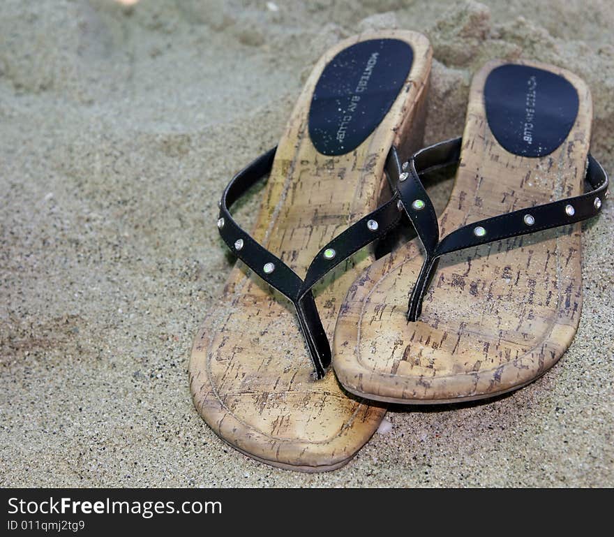 A pair of black sandals on a sandy beach. A pair of black sandals on a sandy beach