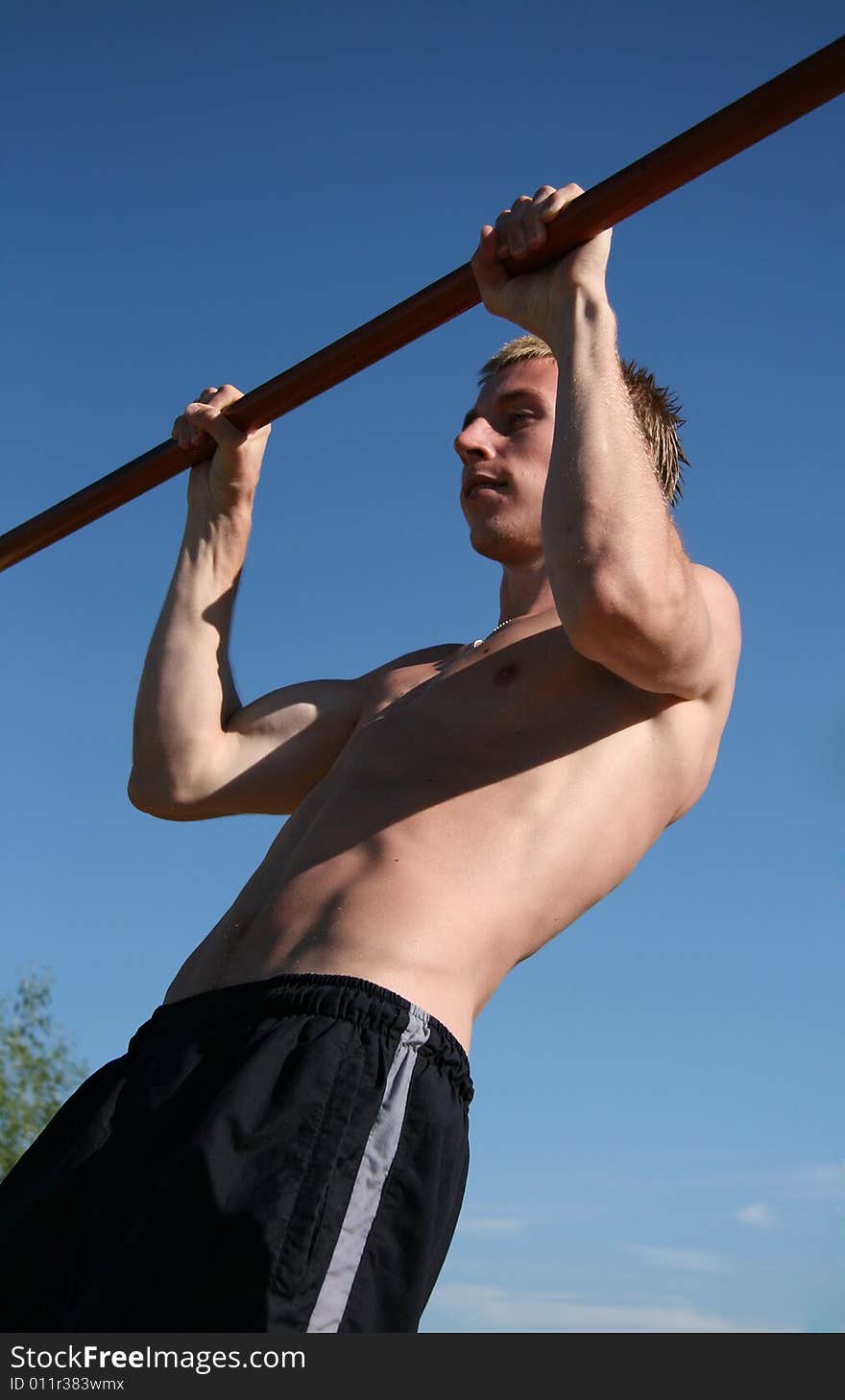 The Young man executes the atheletic exercise on horizontal bar.