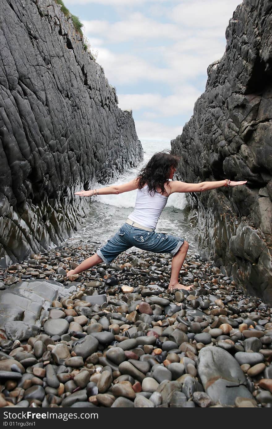 A beautiful woman practicing her yoga on the rocks in a ravine as the waves roll in. A beautiful woman practicing her yoga on the rocks in a ravine as the waves roll in