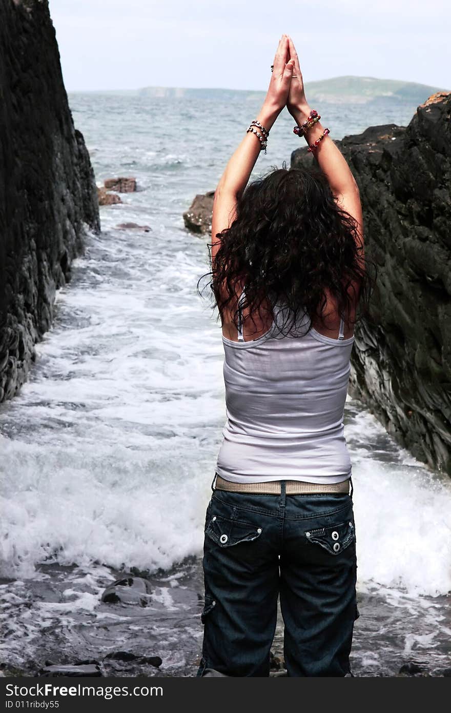 A beautiful woman practicing her yoga on the rocks in a ravine as the waves roll in. A beautiful woman practicing her yoga on the rocks in a ravine as the waves roll in