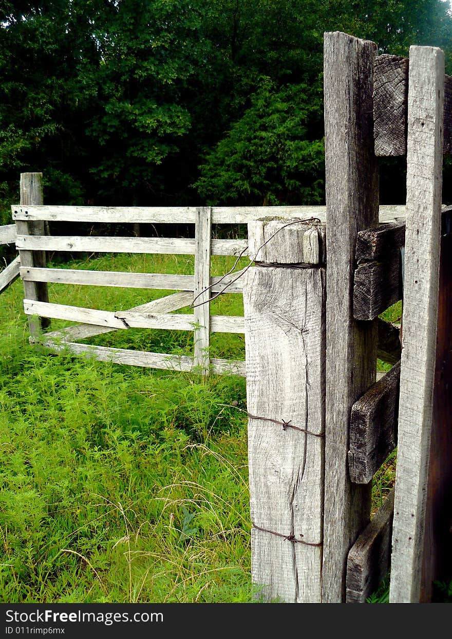 A weathered gray-wood farm fence wrapped with barbed wire. A weathered gray-wood farm fence wrapped with barbed wire