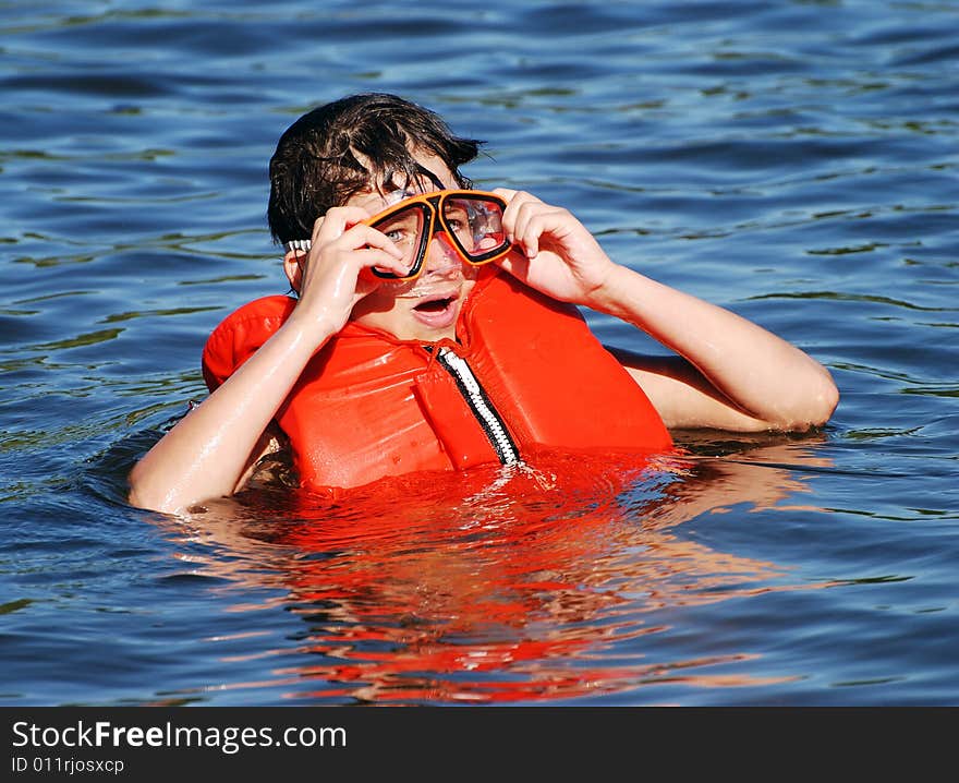 The boy with a life-jacket and a diving mask is ready for a swim in the lake.