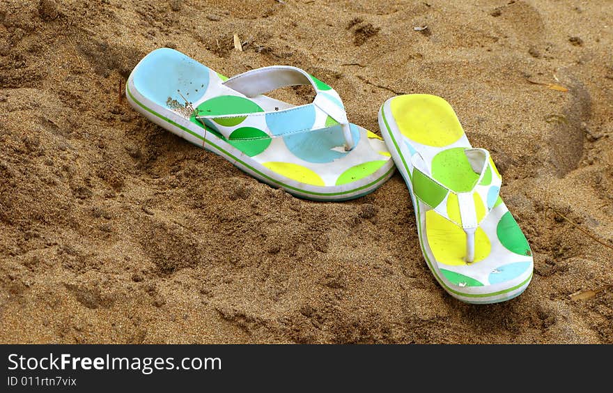 A pair of polka dotted flip flops in the sand.