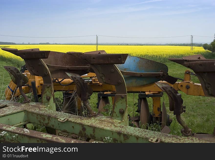 This rusting old plough is set against a vivid yellow field of oilseed rape and a light summer sky. Copy space at top. This rusting old plough is set against a vivid yellow field of oilseed rape and a light summer sky. Copy space at top.