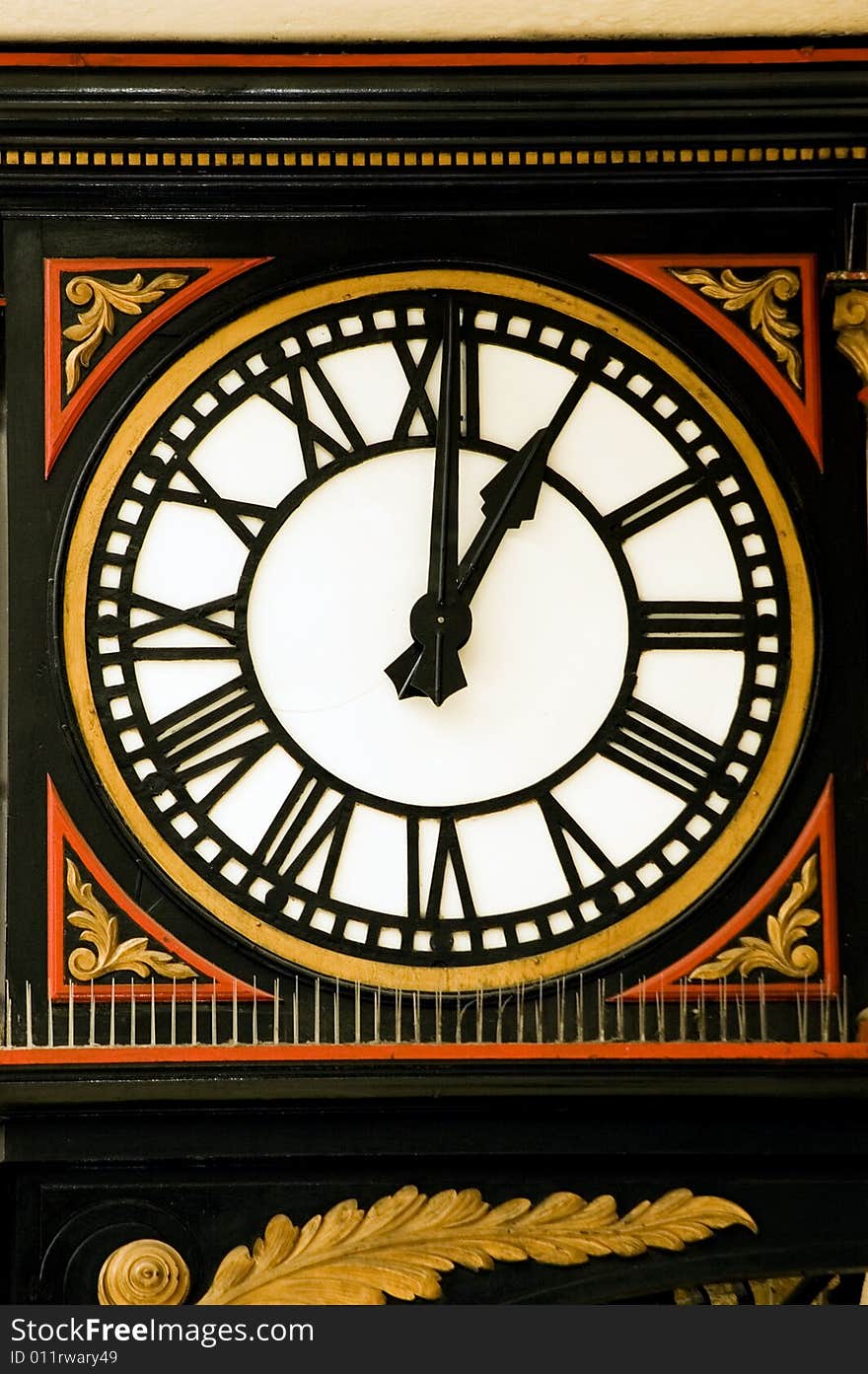 A large decorative station clock [ Charing Cross, London] with Roman numerals in black, gold and red.