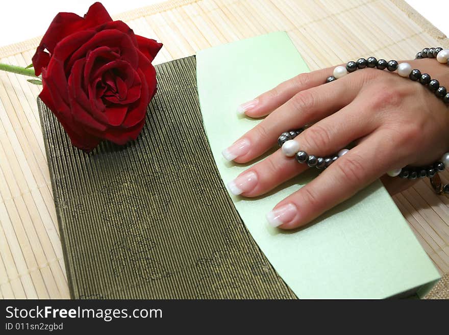 Beautiful long fingers with a good manicure hold beads from black and white pearls and a red rose lies alongside