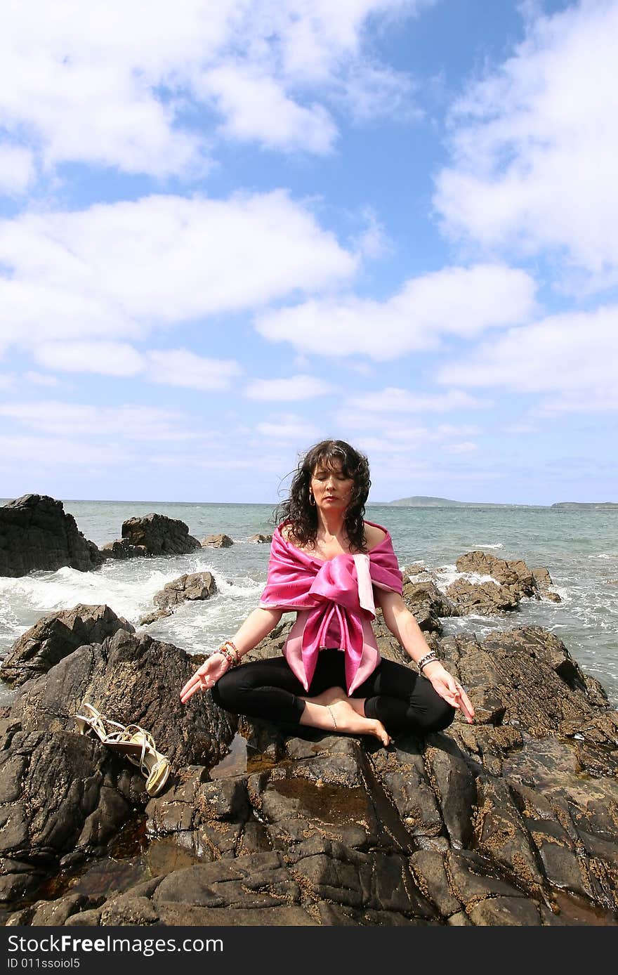 Beautiful woman meditating on the rocks in ireland with her eyes closed, in the lotus position, showing a healthy way to live a happy and relaxed lifestyle in a world full of stress. Beautiful woman meditating on the rocks in ireland with her eyes closed, in the lotus position, showing a healthy way to live a happy and relaxed lifestyle in a world full of stress