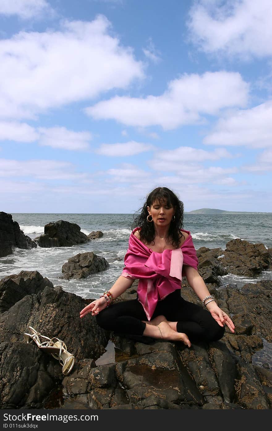 Beautiful woman meditating on the rocks in ireland with her eyes closed, in the lotus position, showing a healthy way to live a happy and relaxed lifestyle in a world full of stress. Beautiful woman meditating on the rocks in ireland with her eyes closed, in the lotus position, showing a healthy way to live a happy and relaxed lifestyle in a world full of stress