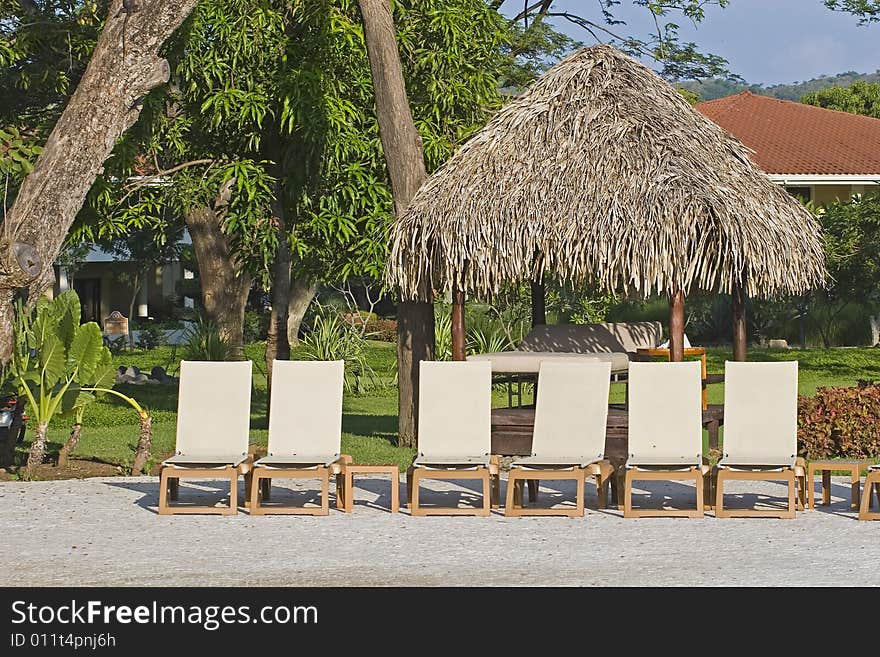 White lounge chairs and a straw hut around a tropical swimming pool. White lounge chairs and a straw hut around a tropical swimming pool