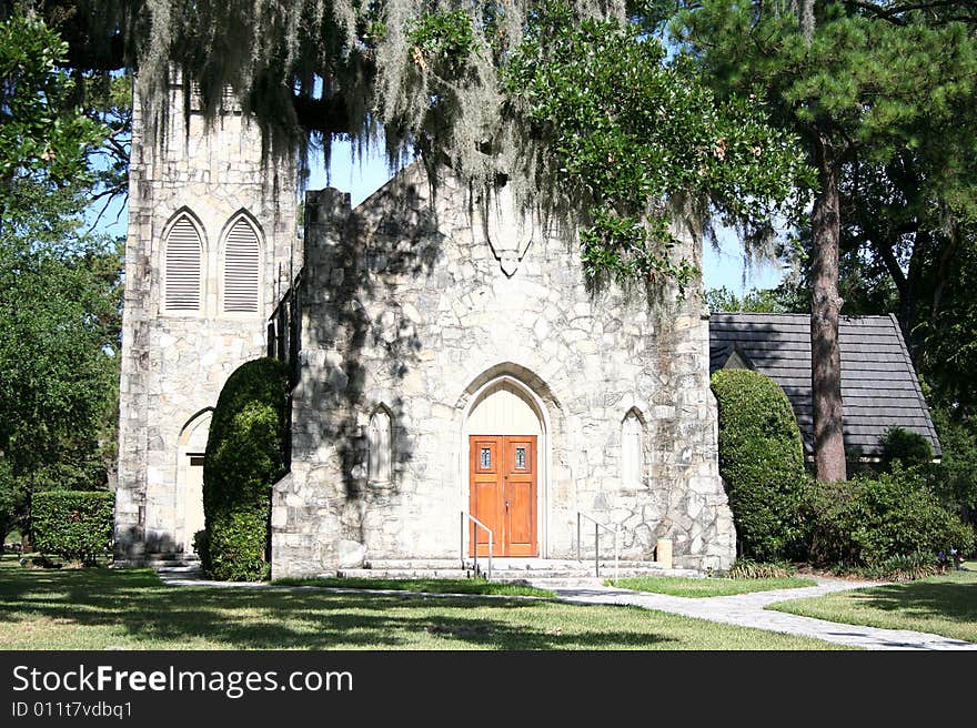 An old stone church sits behind trees with Spanish moss haning down.