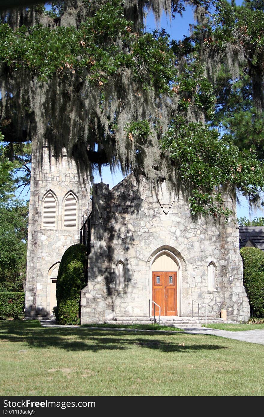 An old stone church sits behind trees with Spanish moss haning down.