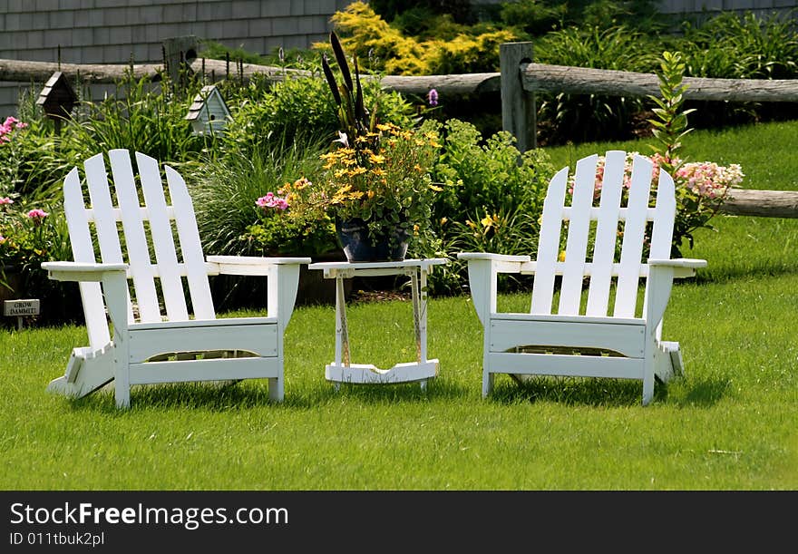 Two white adirondack chairs sit on the lawn ready for someone to sit and enjoy. Two white adirondack chairs sit on the lawn ready for someone to sit and enjoy.