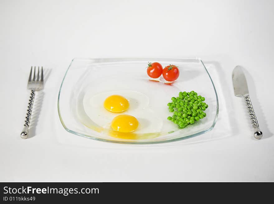 Two raw egg yolk, two cherry tomato and green pees on a plate and isolated on a white background. Two raw egg yolk, two cherry tomato and green pees on a plate and isolated on a white background