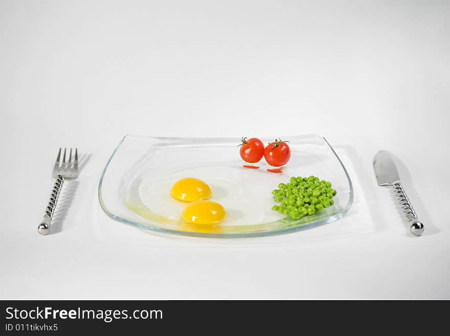 Two raw egg yolk, two cherry tomato and green pees on a plate and isolated on a white background. Two raw egg yolk, two cherry tomato and green pees on a plate and isolated on a white background