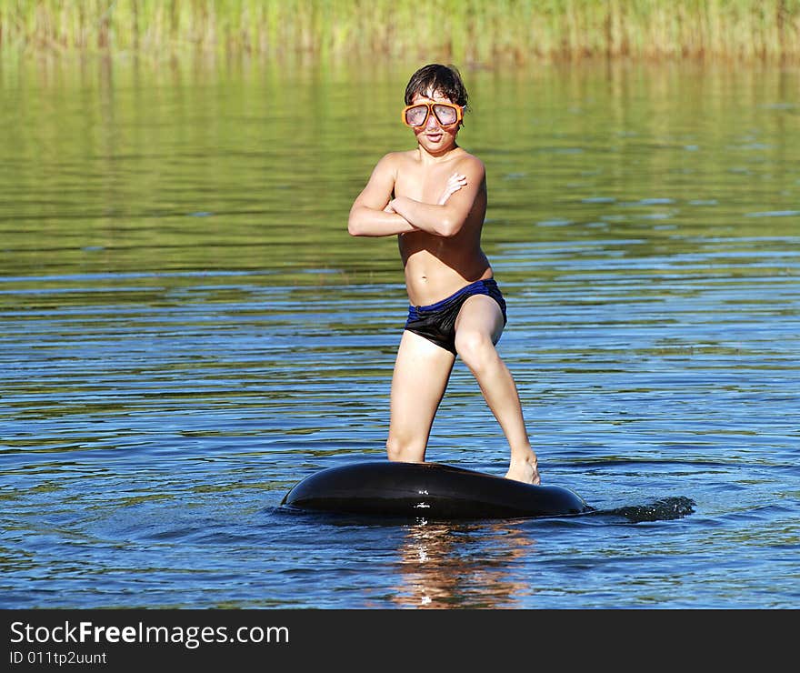 The boy is trying to keep balance on a floating tube while posing. The boy is trying to keep balance on a floating tube while posing.