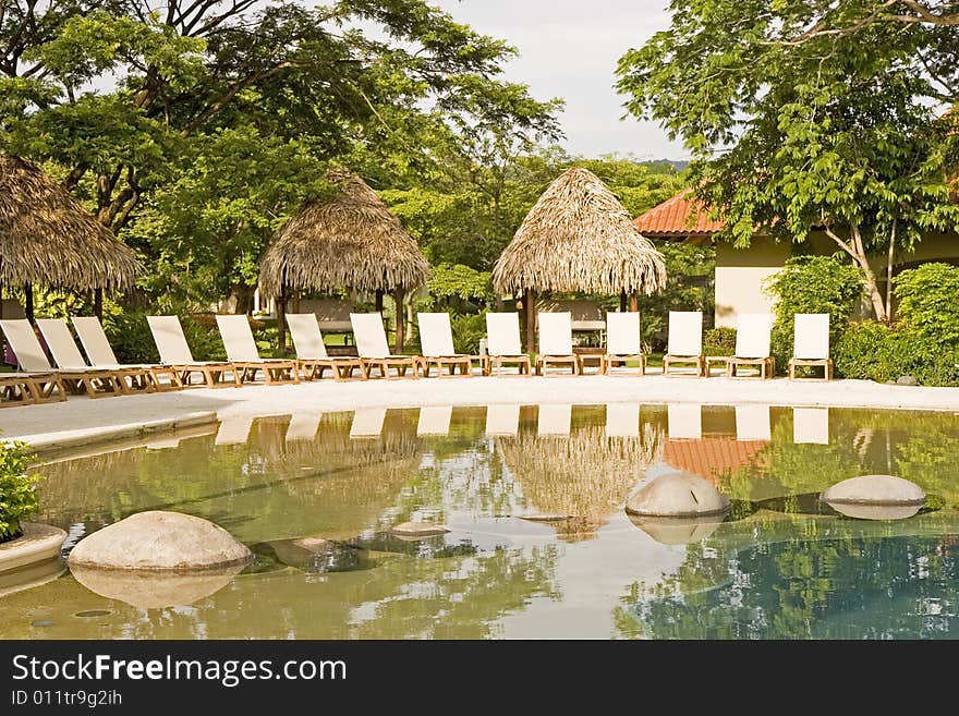 White chaise lounges around a tropical swimming pool. White chaise lounges around a tropical swimming pool