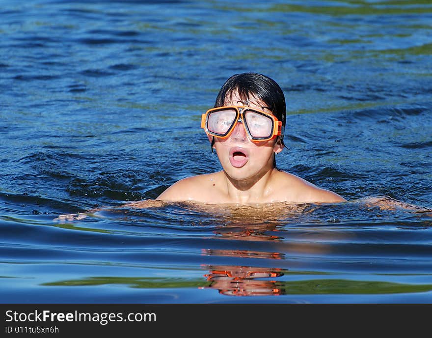 The boy with a misted diving mask swimming in a blue lake water. The boy with a misted diving mask swimming in a blue lake water.