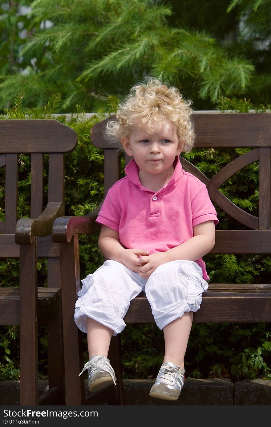 Cute young boy sitting on a bench in summer