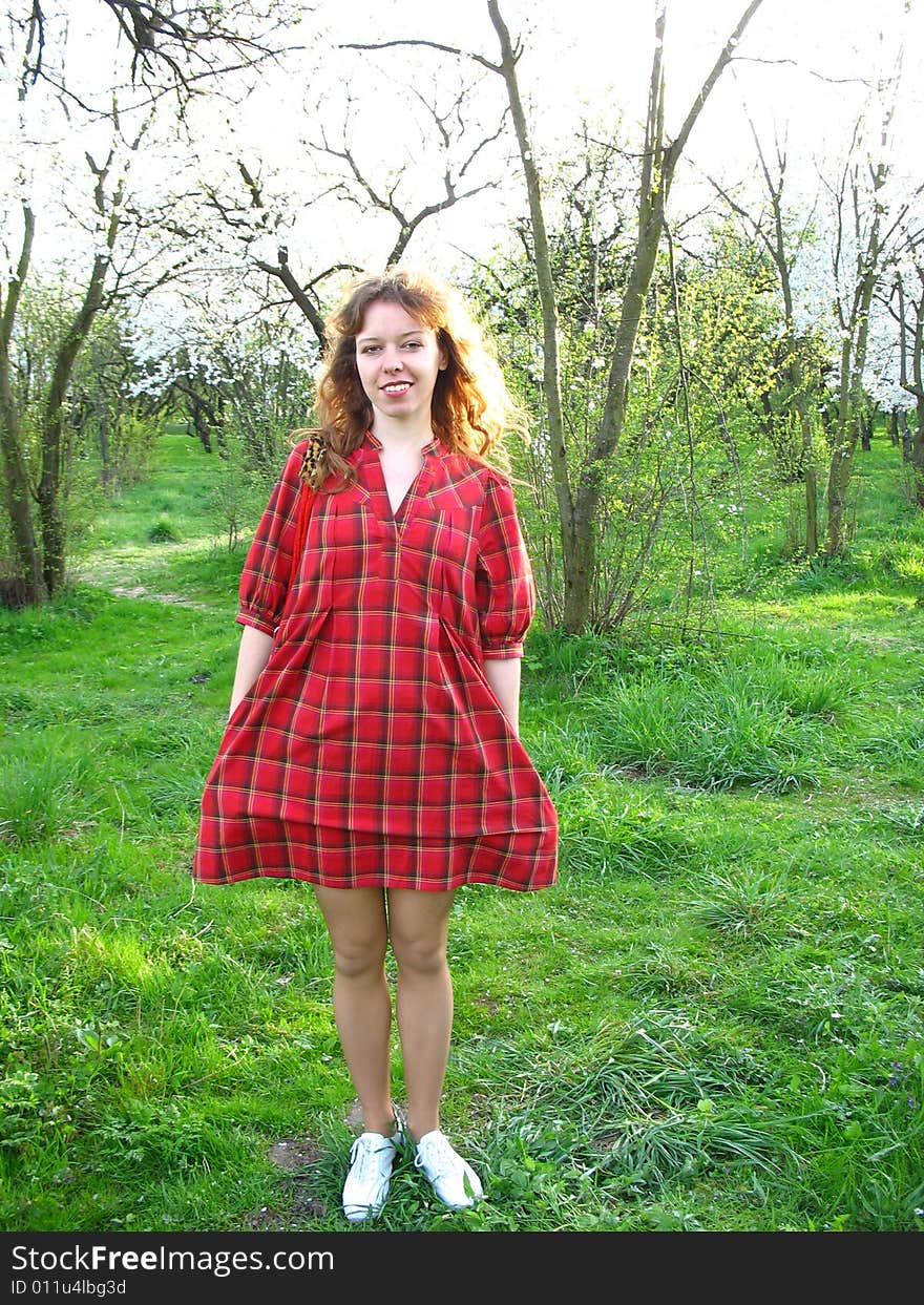 The young red-haired woman is walking through the spring garden. The young red-haired woman is walking through the spring garden