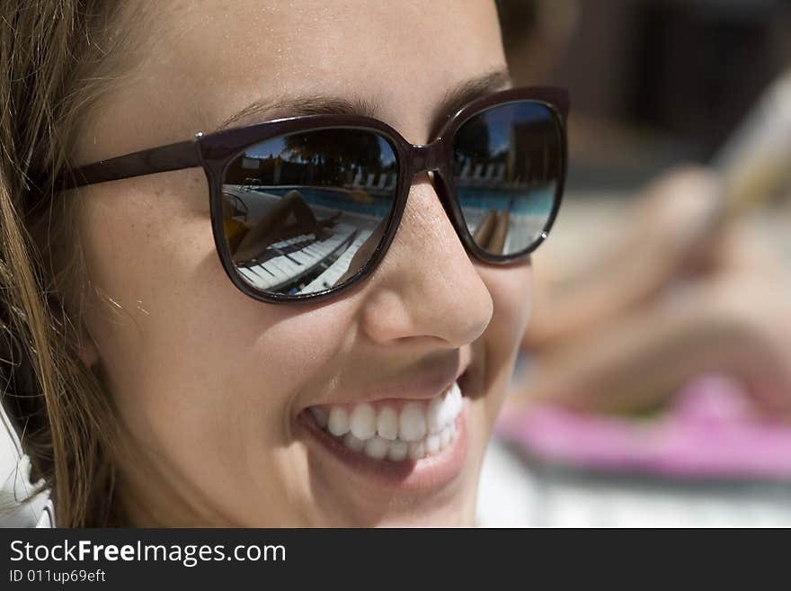 Happy young woman wearing sunglasses, with a reflextion of the pool. Happy young woman wearing sunglasses, with a reflextion of the pool.