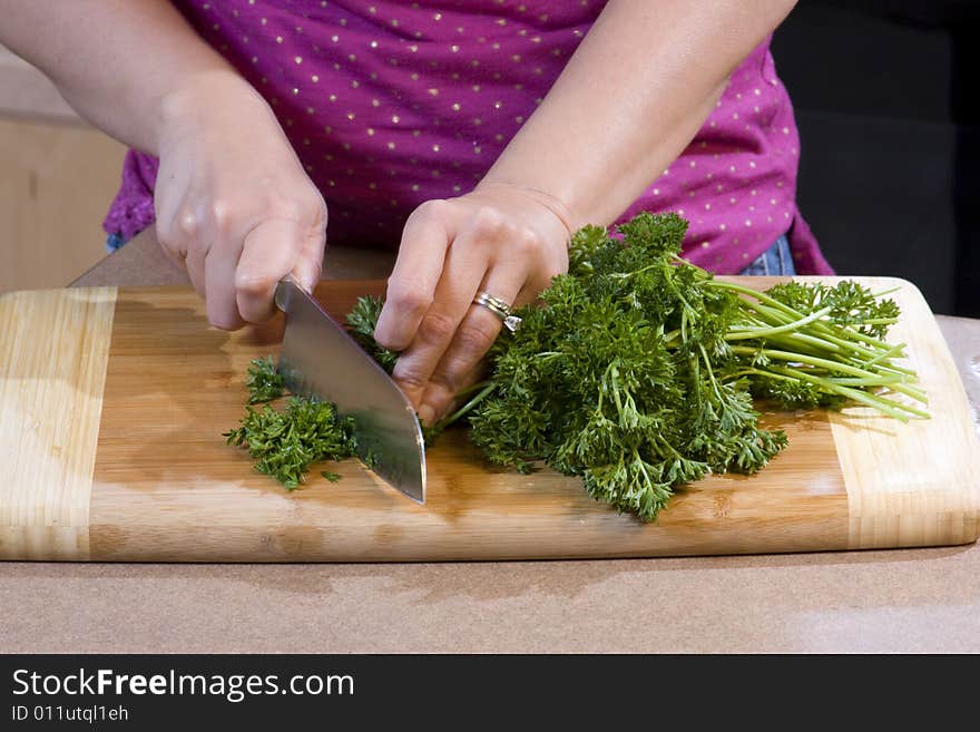 Woman wearing a pink shirt chopping food on a bamboo cutting board with a chef's knife. Woman wearing a pink shirt chopping food on a bamboo cutting board with a chef's knife.