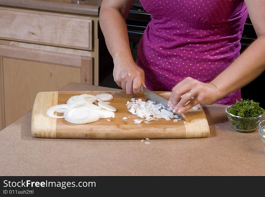 Woman wearing a pink shirt chopping onions on a bamboo cutting board with a chef's knife. Woman wearing a pink shirt chopping onions on a bamboo cutting board with a chef's knife.