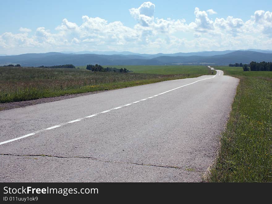 Landscape with the asphalted empty road, taking place waves on hills, clouds, the sky, mountains in distances. Beauty and calmness. Landscape with the asphalted empty road, taking place waves on hills, clouds, the sky, mountains in distances. Beauty and calmness.