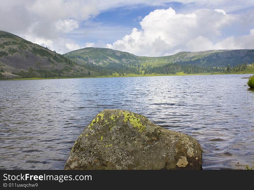 Kind on mountain lake. A stone with a lichen in the foreground.