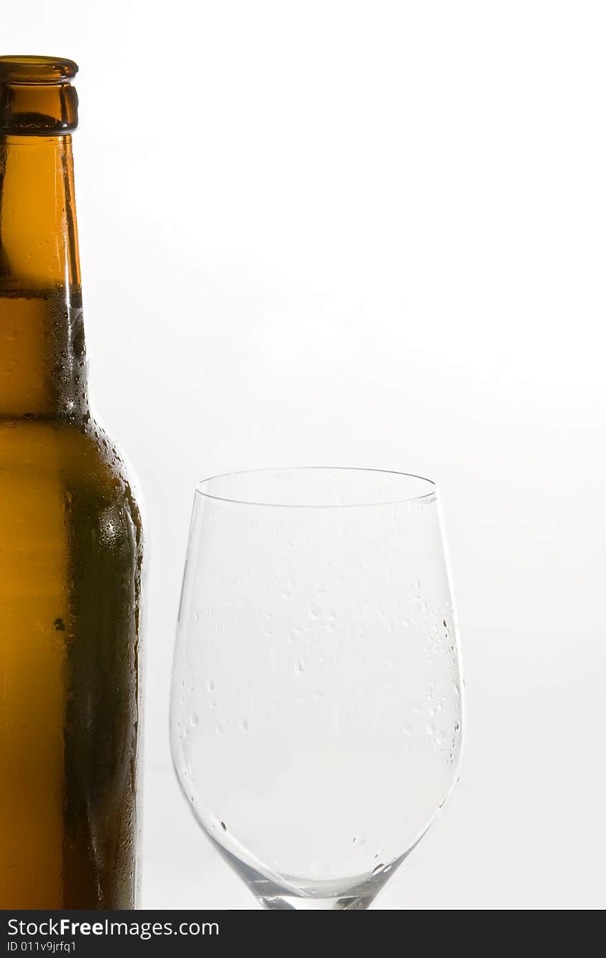 A open beer-bottle is standing next to an empty beer-glass. A open beer-bottle is standing next to an empty beer-glass