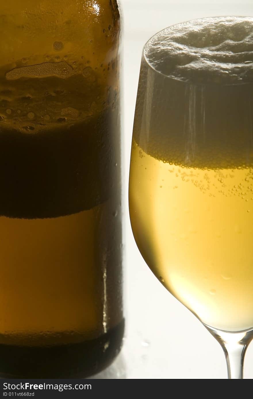 A open beer-bottle is standing next to an empty beer-glass. A open beer-bottle is standing next to an empty beer-glass