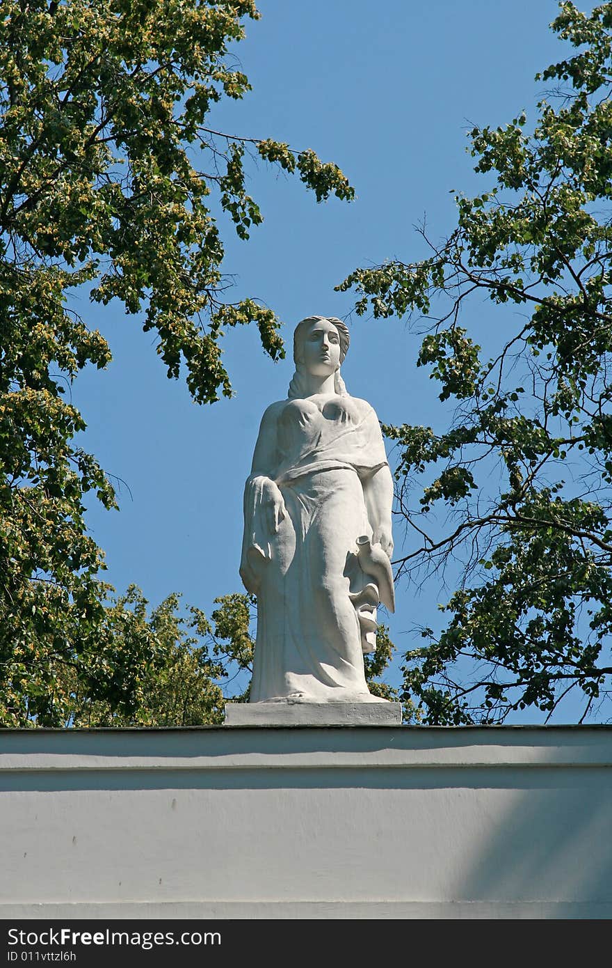 Sculpture on a background of the sky in a frame of branches of a tree