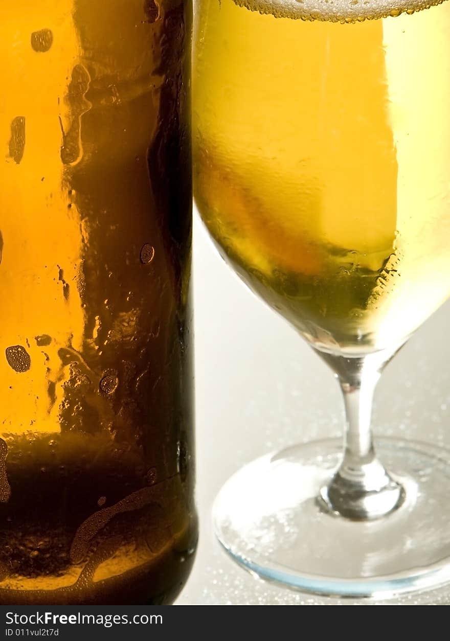 A open beer-bottle is standing next to an empty beer-glass. A open beer-bottle is standing next to an empty beer-glass