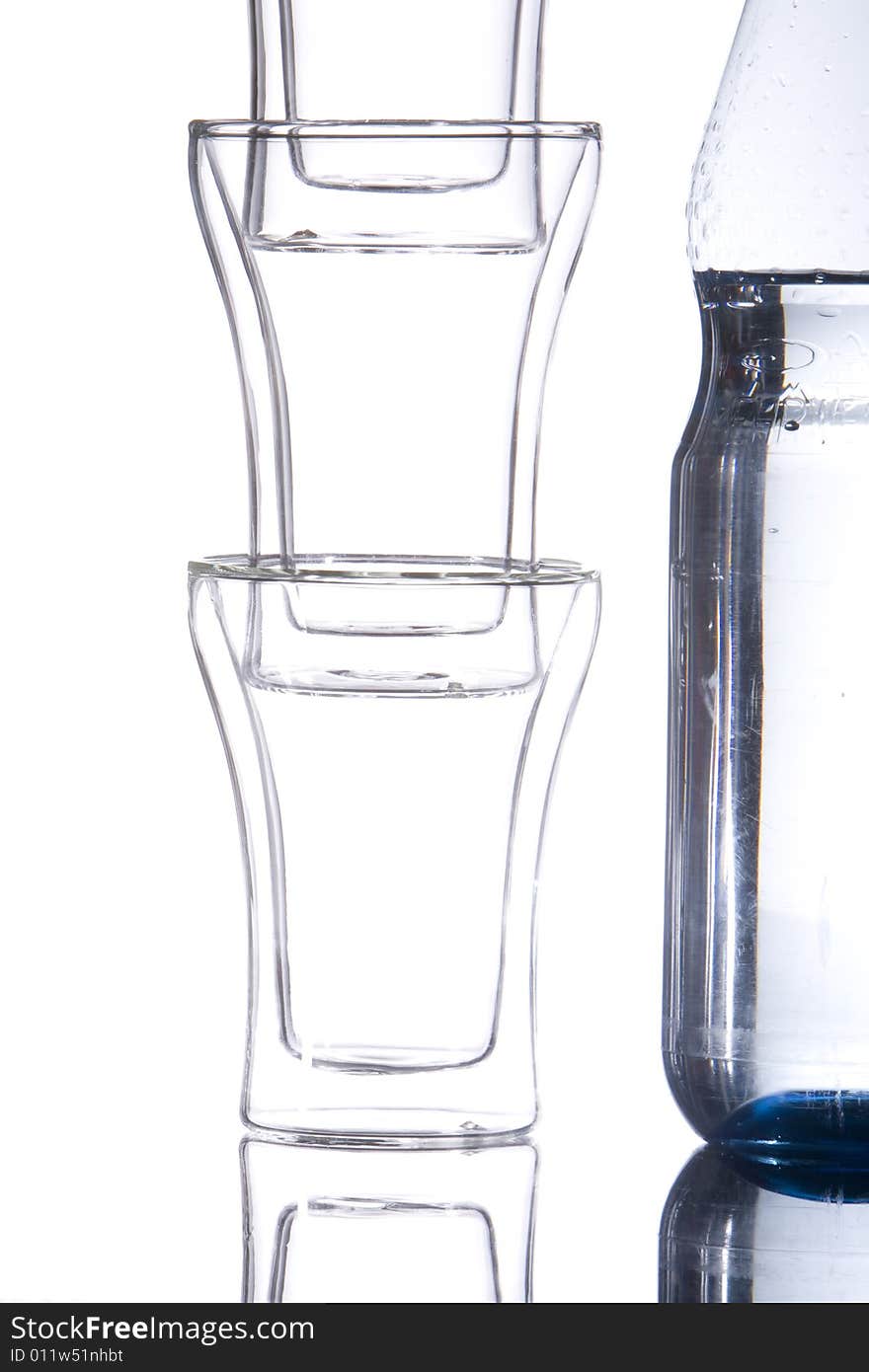 A bottle of mineralwater with three piled glasses.