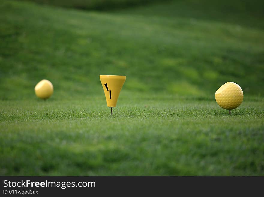 Close view of two yellow balls on a tee in front of a green background. Close view of two yellow balls on a tee in front of a green background