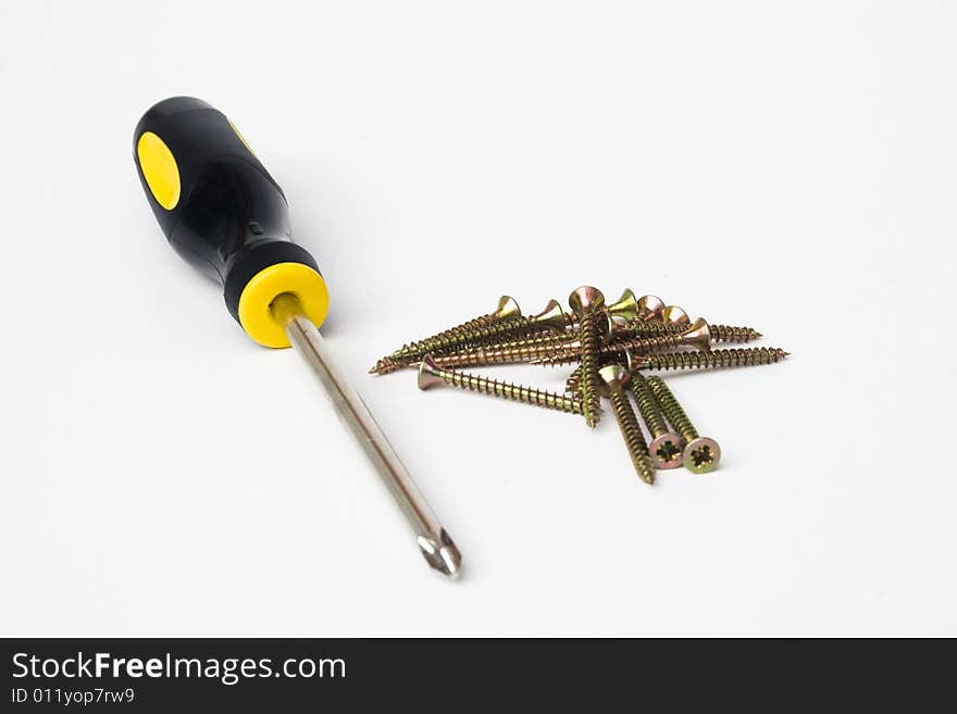 Yellow and black handled phillips screwdriver with pile of screws on white background. Yellow and black handled phillips screwdriver with pile of screws on white background