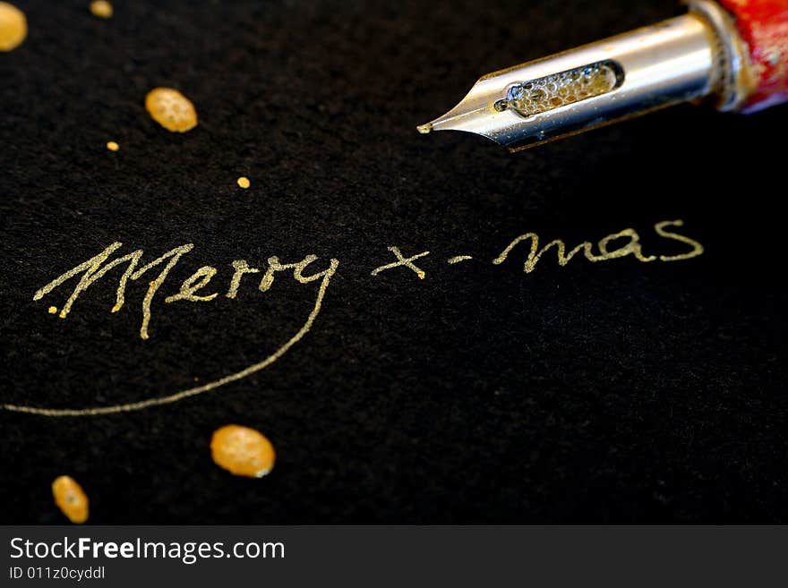 Ink feather with golden handwriting. Text :Merry x-mas on black background with drips. Ink feather with golden handwriting. Text :Merry x-mas on black background with drips