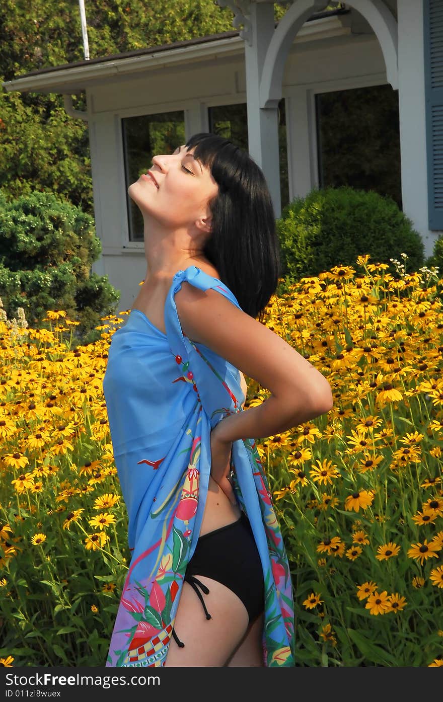 Young beautiful woman in an black bikini standing in front of a field of yellow 
flowers in the sunset, and a nice blue big scarf on. Young beautiful woman in an black bikini standing in front of a field of yellow 
flowers in the sunset, and a nice blue big scarf on.