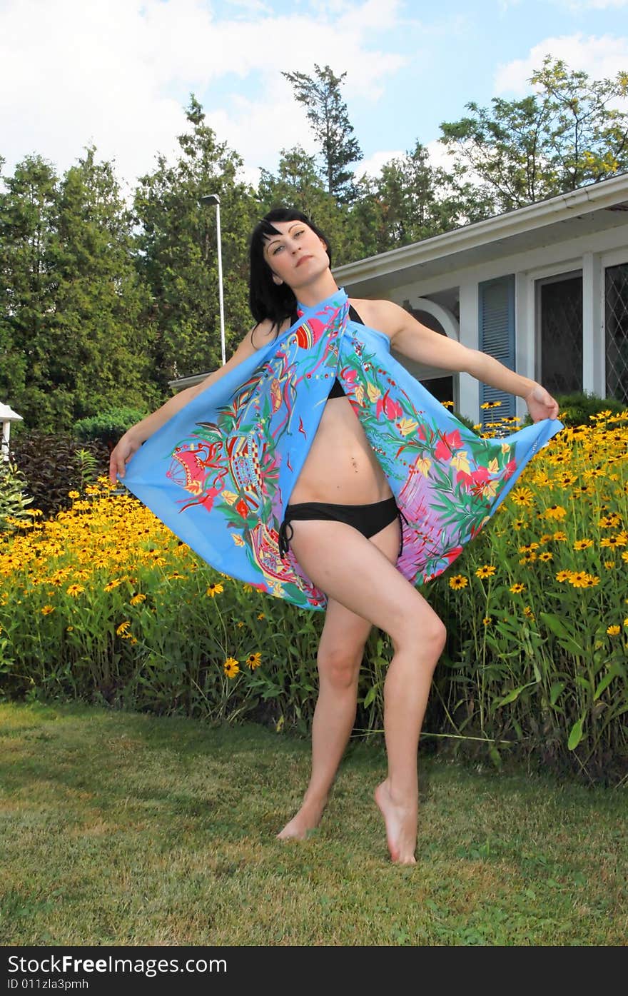 Young beautiful woman in an black bikini standing in front of a field of yellow 
flowers in the sunset, and a nice blue big scarf on. Young beautiful woman in an black bikini standing in front of a field of yellow 
flowers in the sunset, and a nice blue big scarf on.