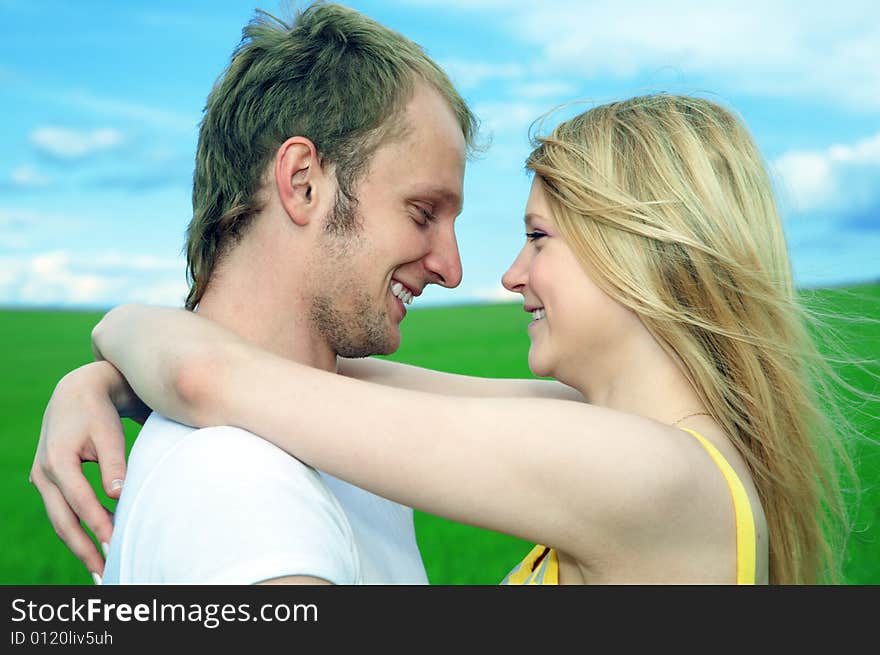 Young love couple embrace in field under blue sky