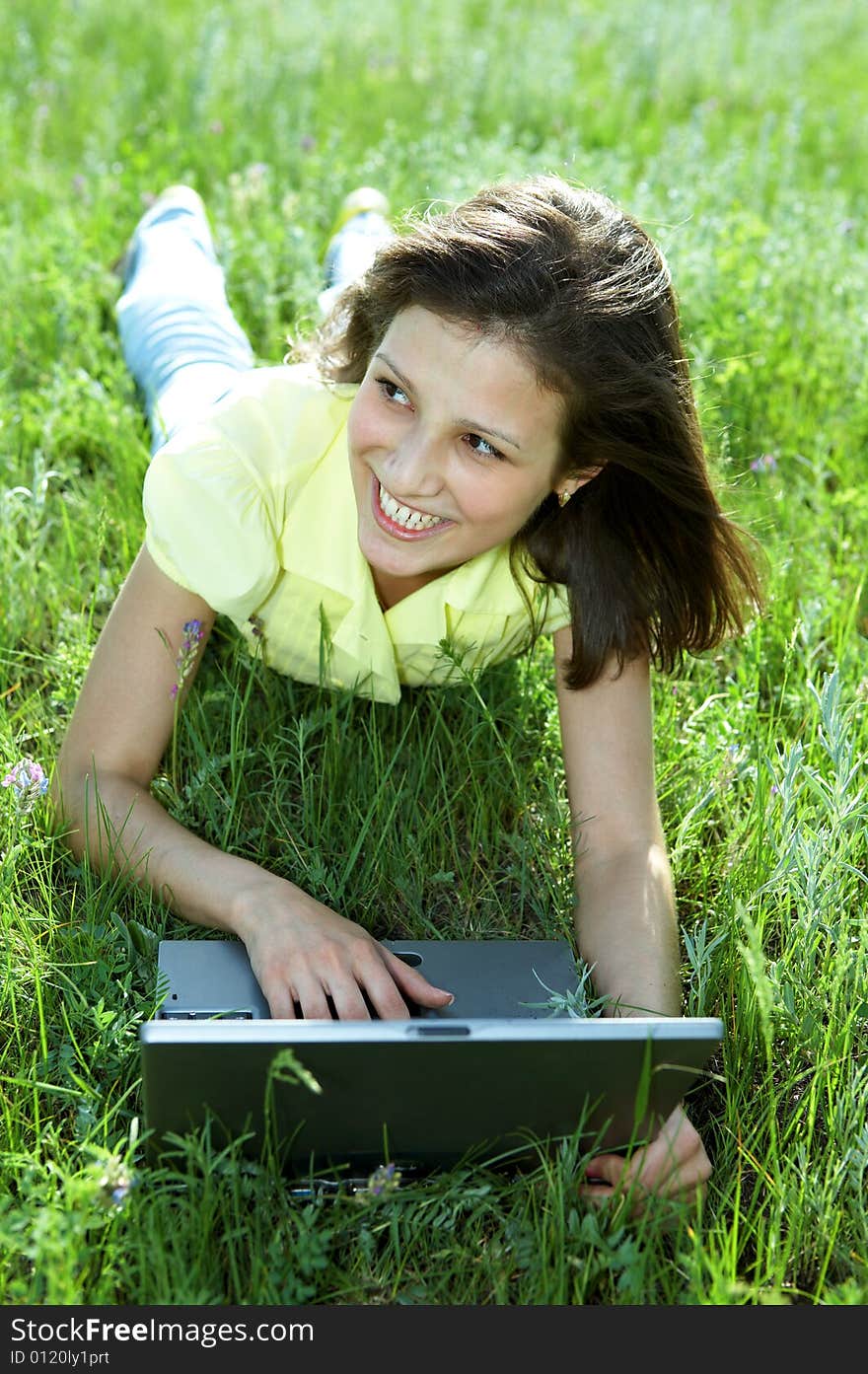 Pretty woman with laptop on the green grass under blue sky