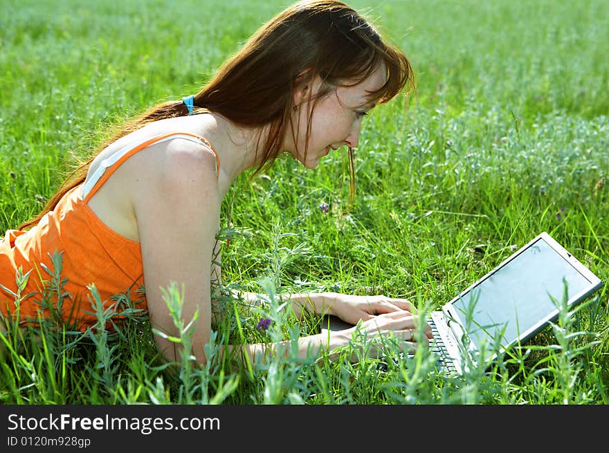 Pretty woman with laptop on the green grass under blue sky