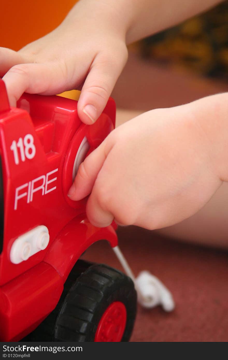 Toddler playing with a toy fire truck turning know to roll up fire hose. Toddler playing with a toy fire truck turning know to roll up fire hose